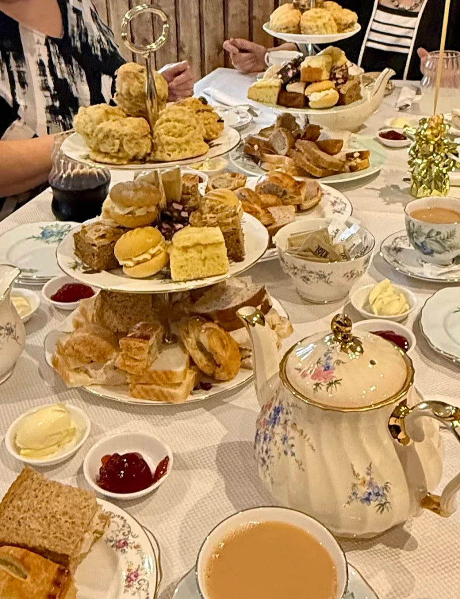 Afternoon tea stand with sandwiches, scones and cakes alongside a vintage floral teapot
