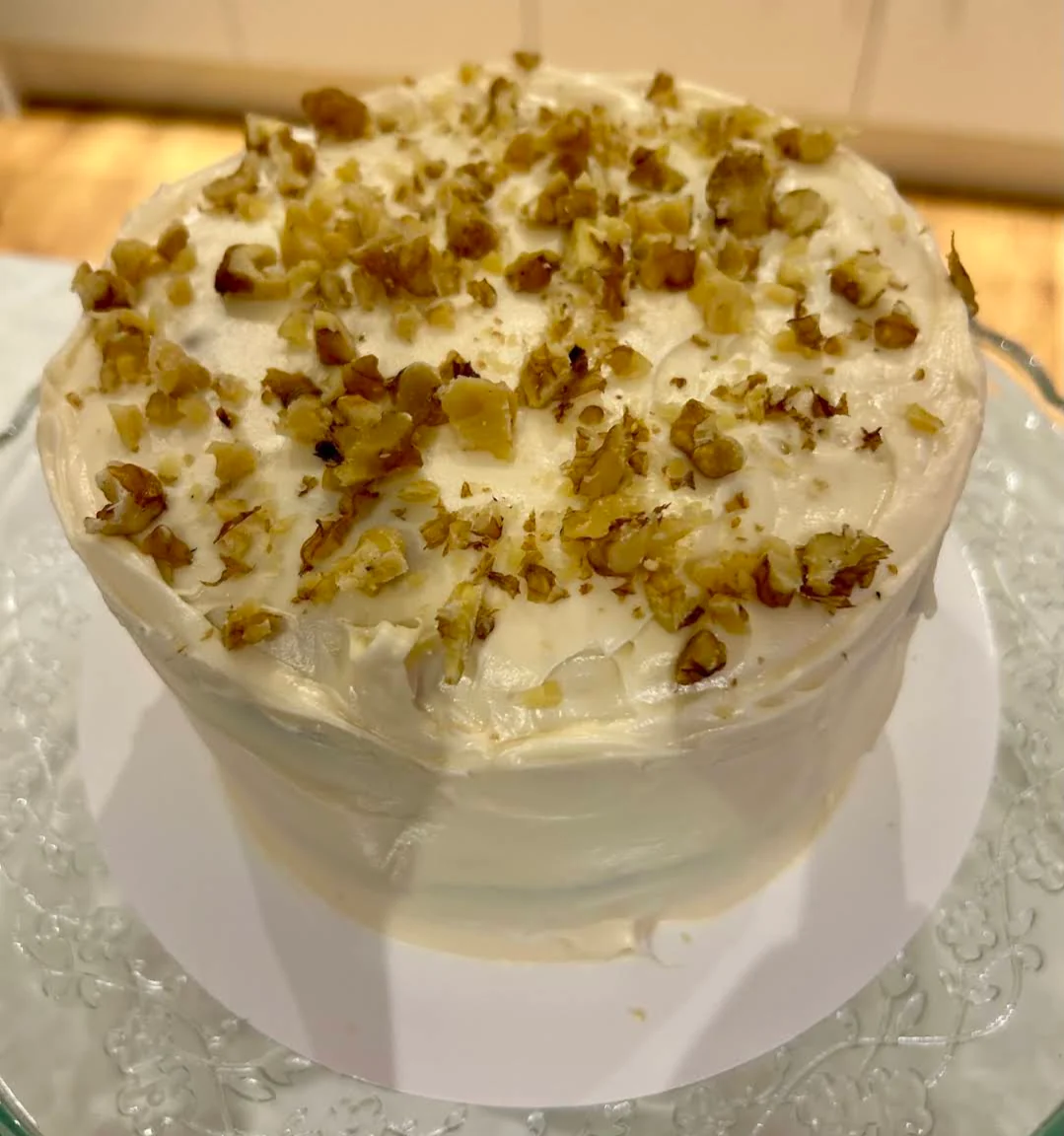 A large homemade cake topped with cream cheese frosting and chopped nuts